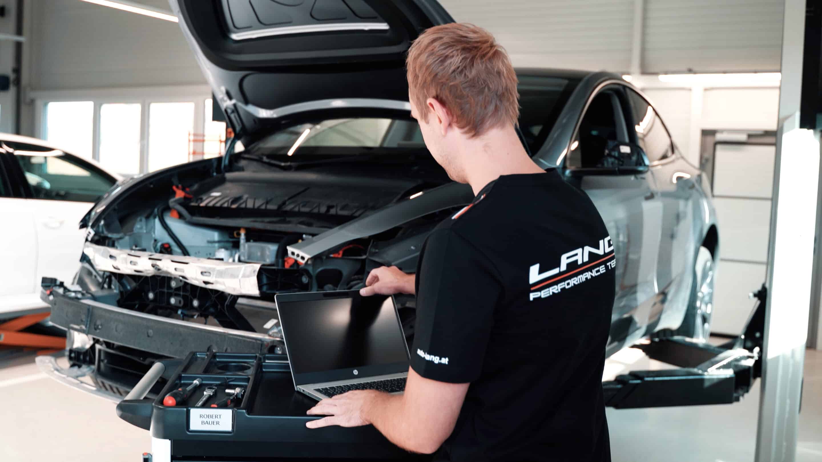 Ein Mitarbeiter von Auto Lang steht vor einem Tesla um diesen für die Reparatur zu überprüfen.