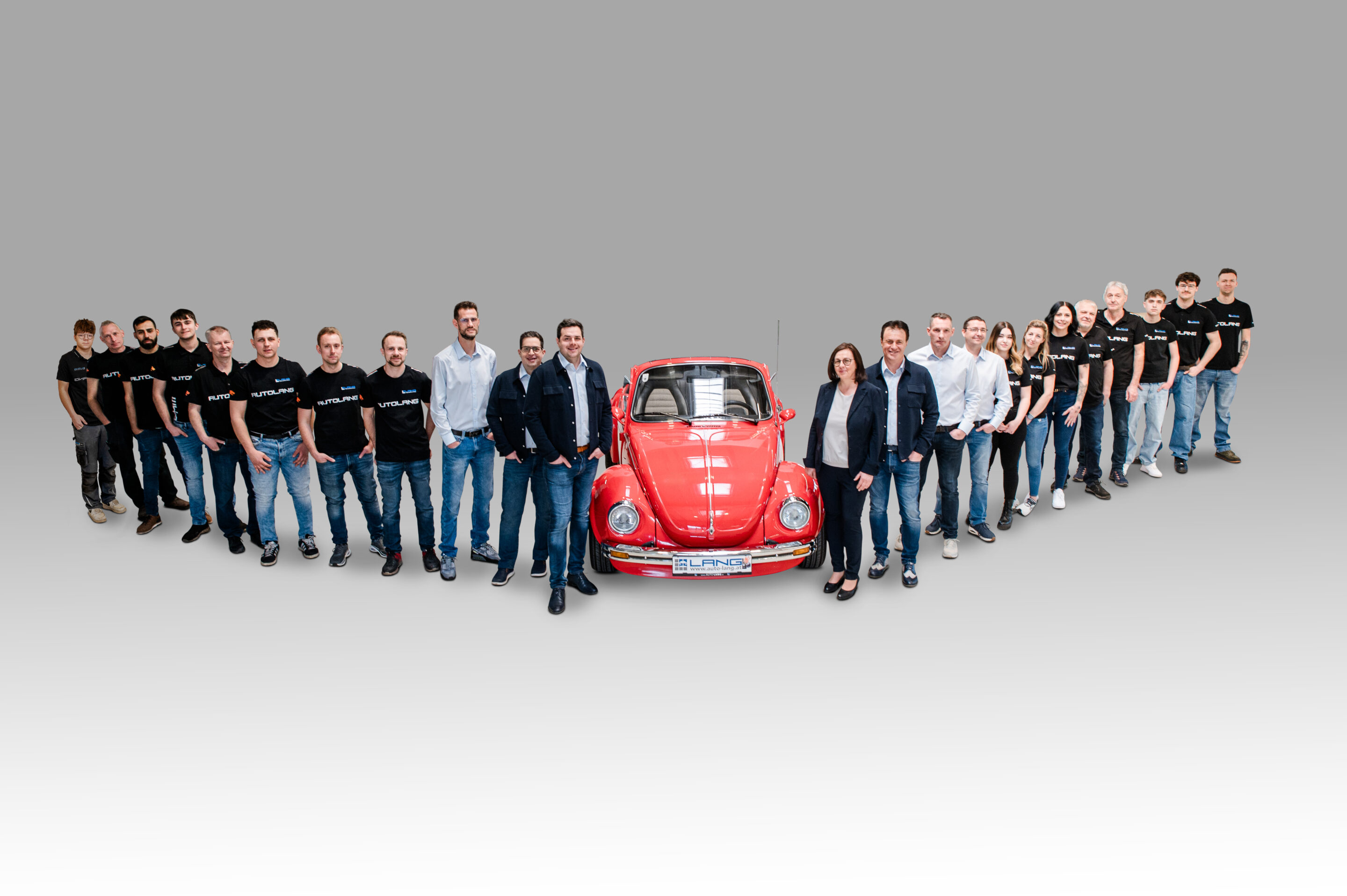 Das Autohaus Lang Team steht versammelt um einen roten VW Käfer